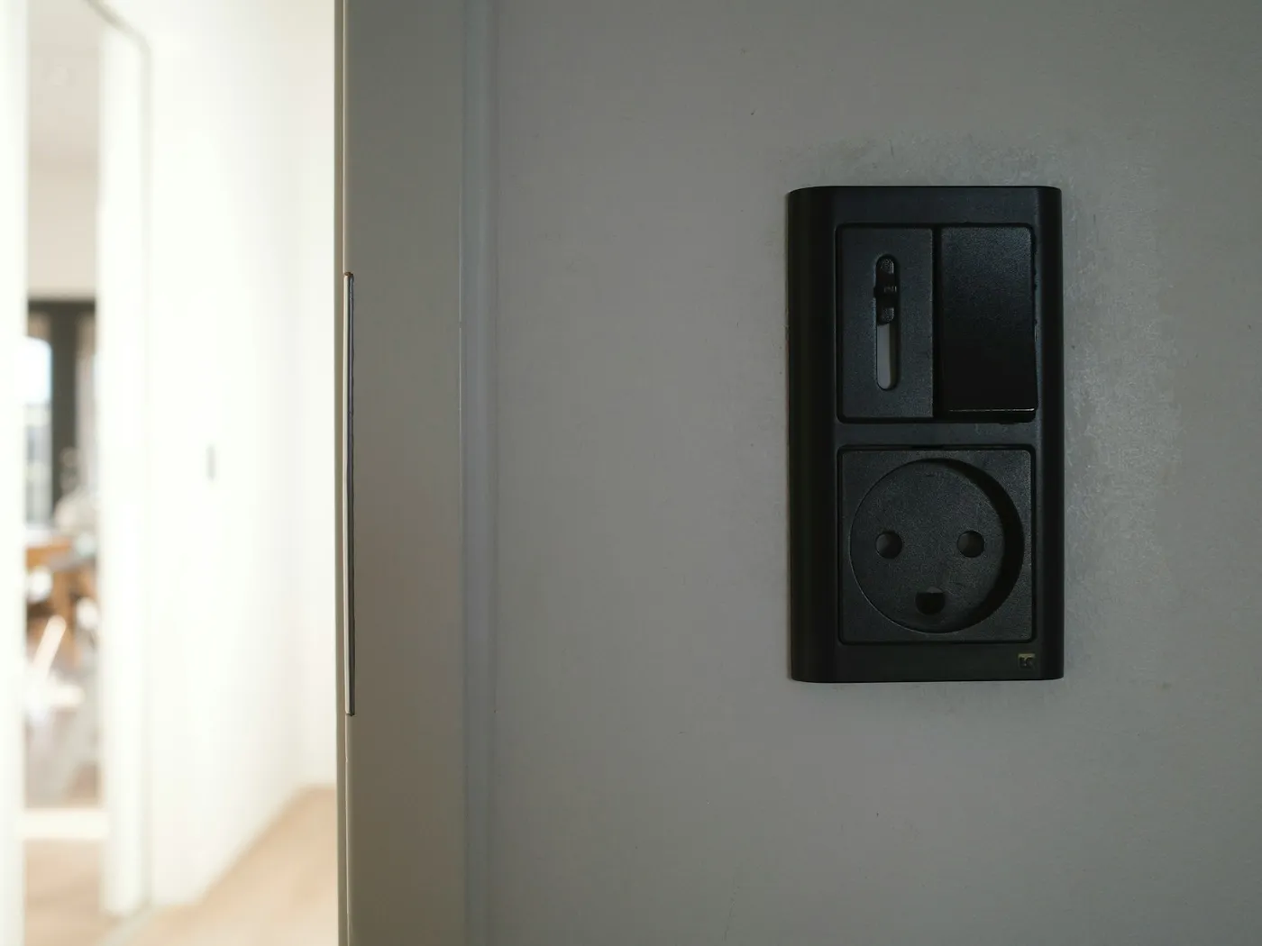 A black European wall socket beside a bright doorway in a rented apartment