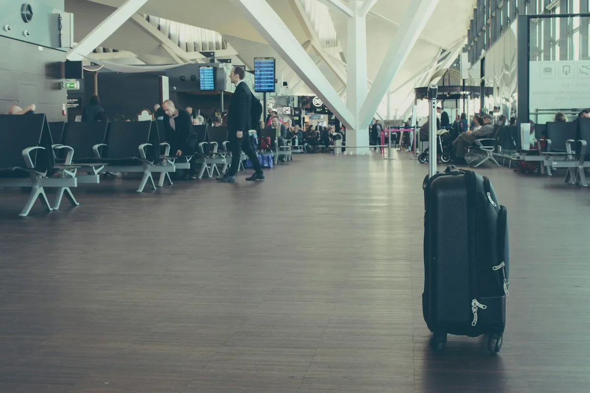A black wheeled suitcase with visible zipper pulls standing in an airport terminal