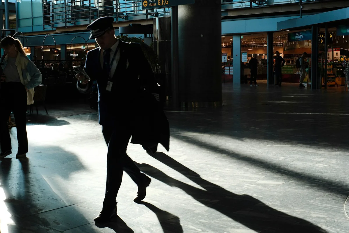 A uniformed airline crew member walking through a sunlit airport terminal