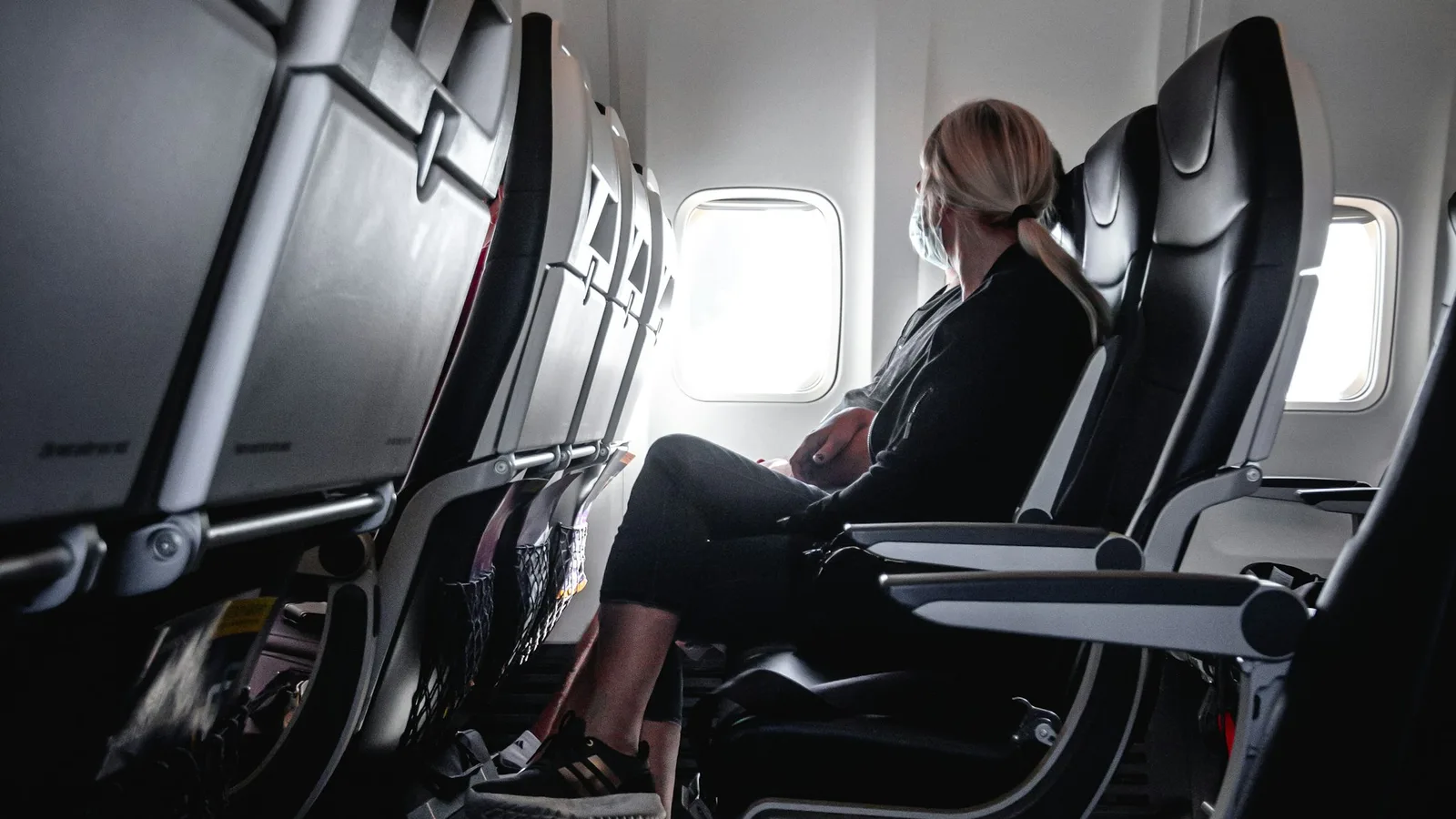A traveler resting in an airplane seat beside the window in a quiet cabin