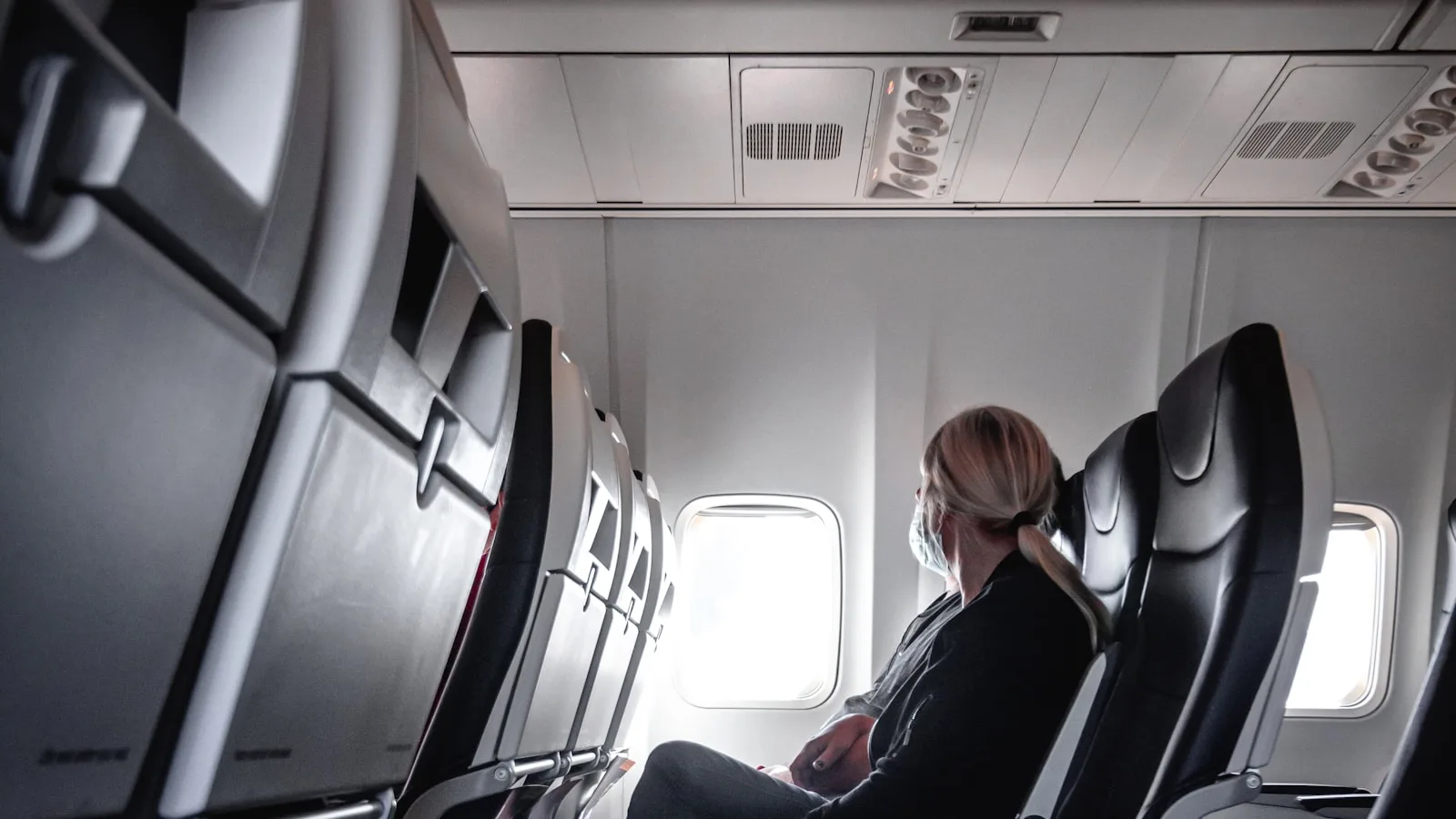 A lone passenger resting beside a bright window in a quiet airplane cabin
