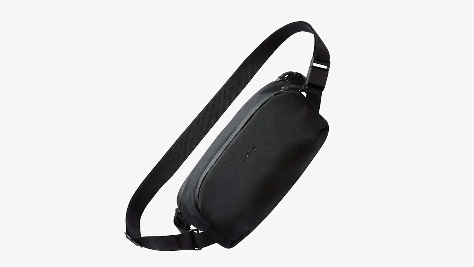 A black Bellroy Venture Ready sling bag suspended by its webbing strap against a plain light background