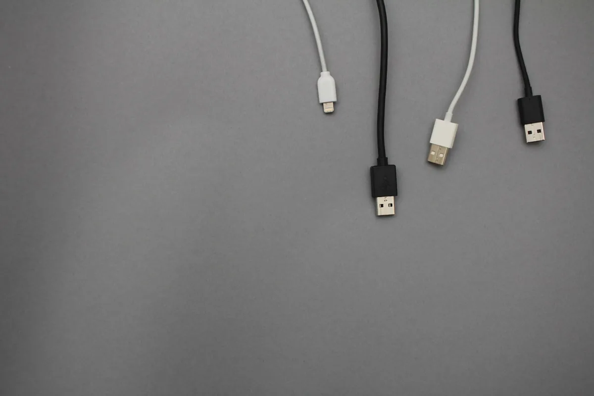 An assortment of black and white charging cables and cords laid out flat on a light surface, the tangle a travel cable organizer is meant to solve
