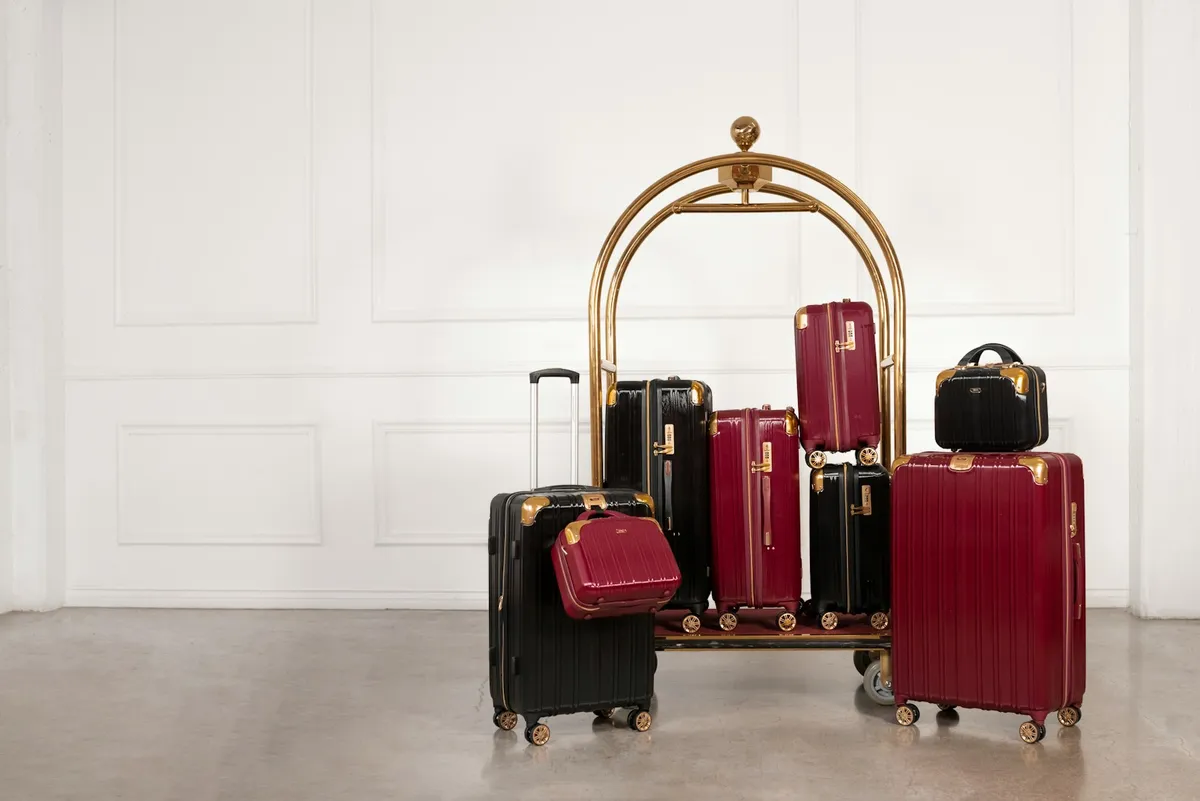 Black and burgundy hardside suitcases of different sizes arranged on a brass hotel luggage cart