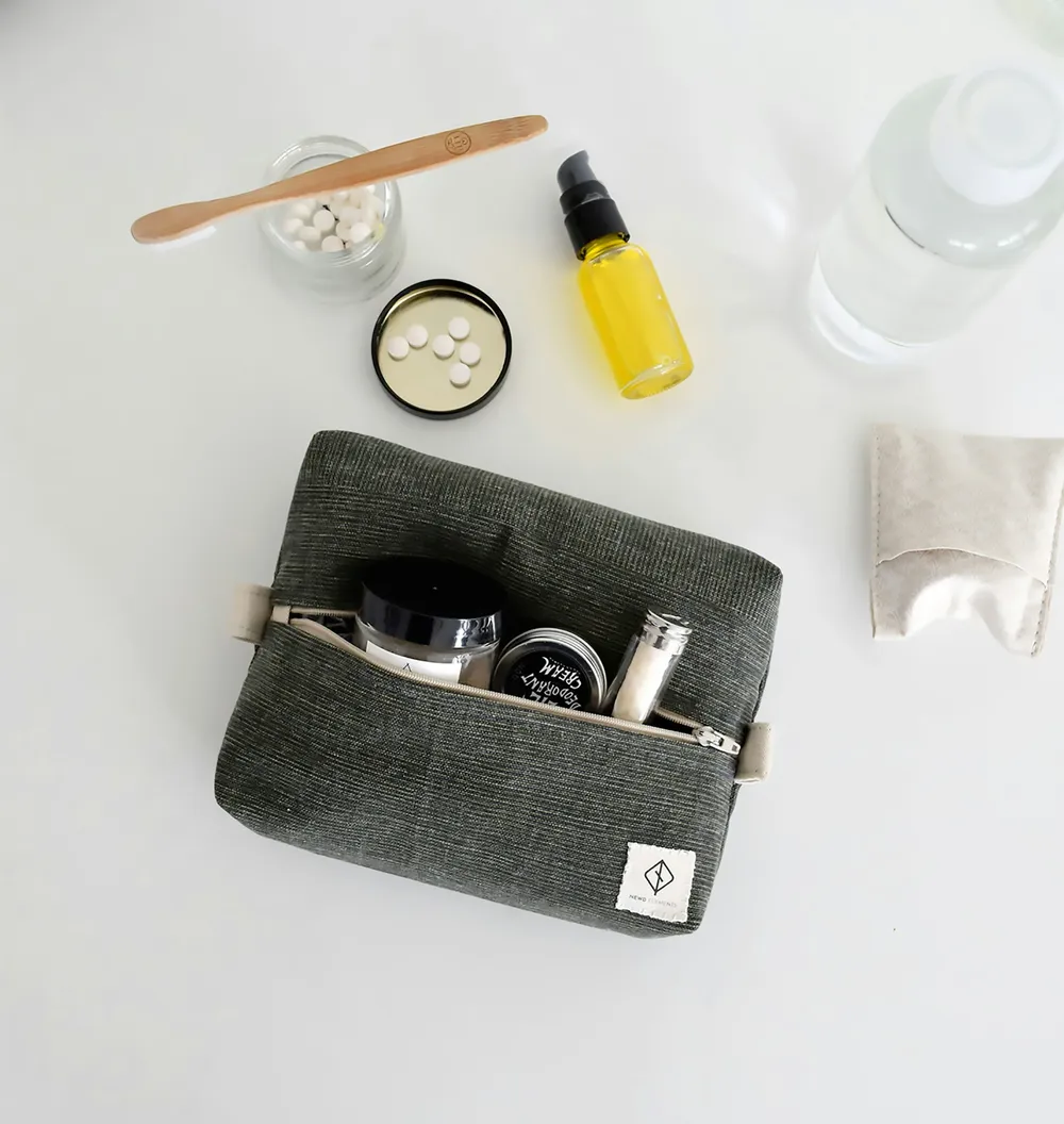 A grey woven dopp kit sitting open on a white surface, surrounded by grooming products, a toothbrush, and a bottle of oil