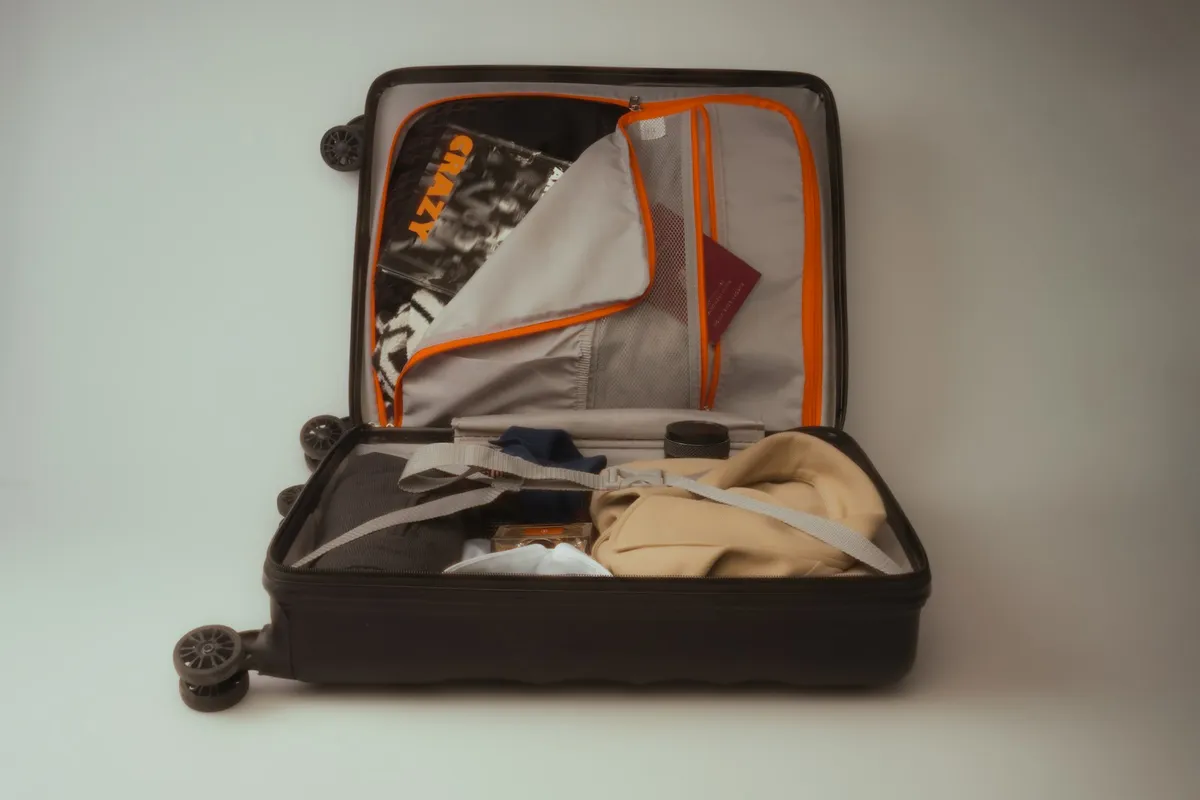 An open black carry-on suitcase packed with folded clothes, a strap, and travel items