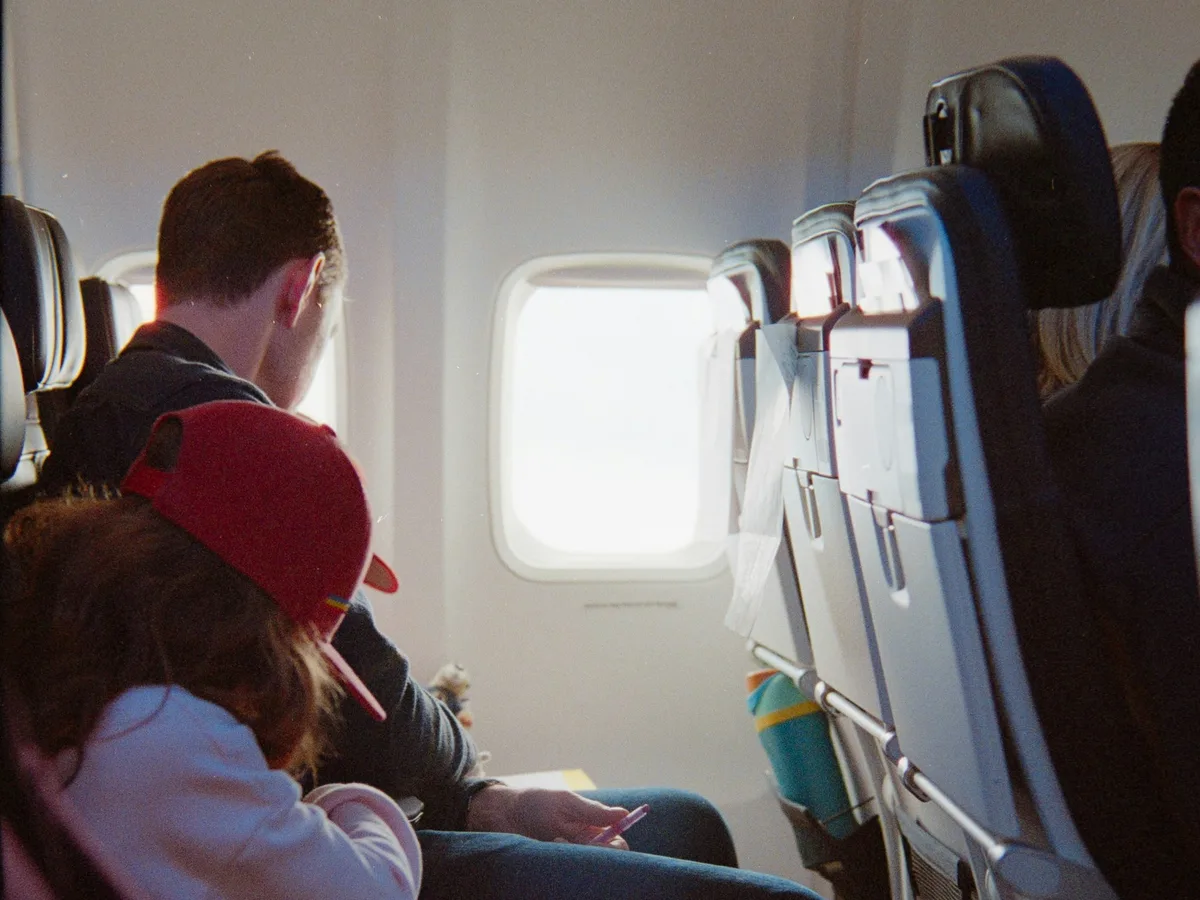 A child resting her head against her seatmate's arm in an airplane cabin