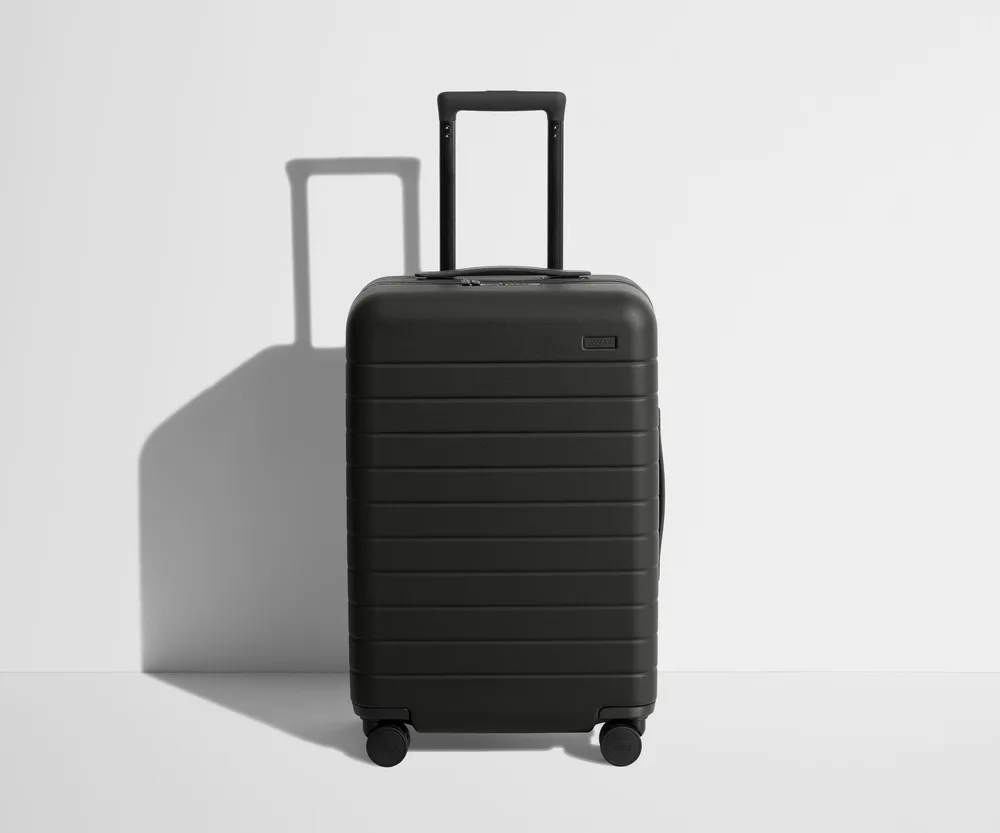 The Away Bigger Carry-On hardside spinner suitcase in jet black, standing upright with its telescoping handle down