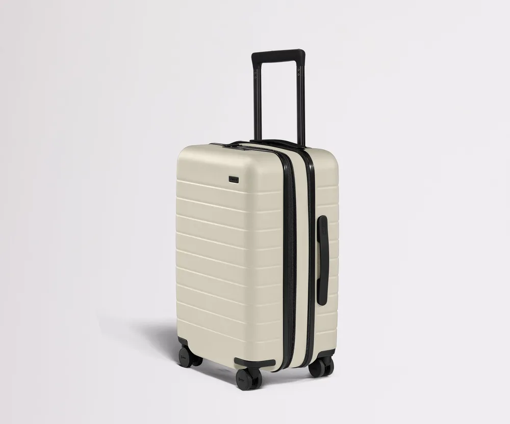 The Away Carry-On Flex expandable hardside spinner suitcase in salt white, with its expansion zipper running around the shell