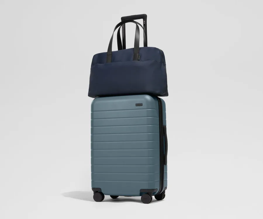 An Away hardside carry-on in slate blue with a navy weekender bag sitting on top, sold together as a bundle