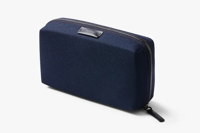 The Bellroy Tech Kit in navy, a slim flat clamshell tech organizer with leather accents opened to show elastic loops and a card slot