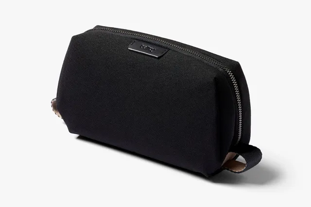 The Bellroy Toiletry Kit in black, a slim woven dopp kit with a wide horseshoe zipper opened to show the interior mesh pocket