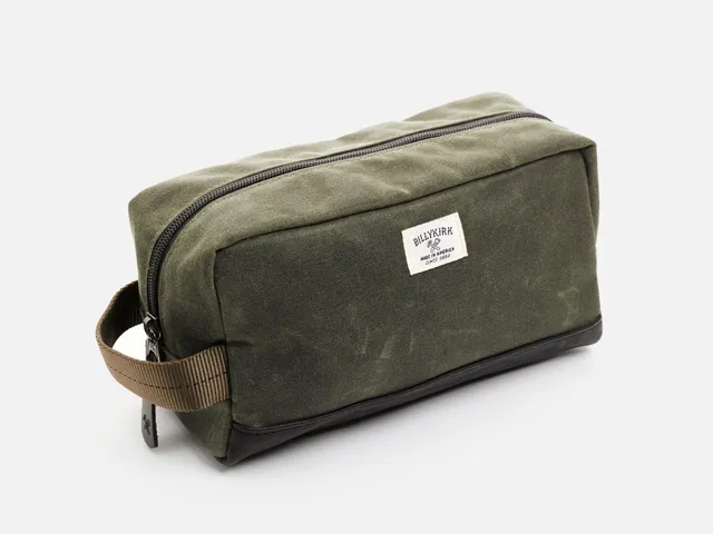 The Billykirk No. 258 toiletry bag in olive waxed canvas with a full-grain leather base and trim, zipped closed with a leather pull
