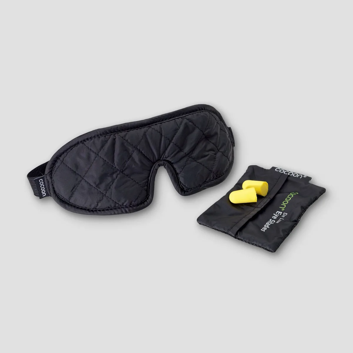 The quilted black Cocoon Eye Shade sleep mask beside its pouch and yellow foam earplugs