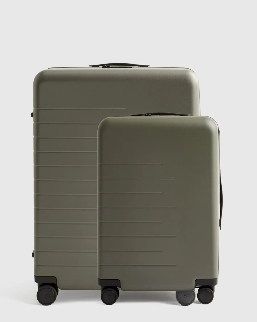 The Quince hard shell suitcase bundle in olive green, a carry-on spinner standing in front of a larger check-in suitcase