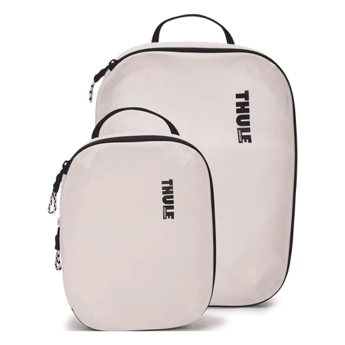 The Thule Compression Cube Set in white, a small and a medium compression packing cube standing upright with black zippers