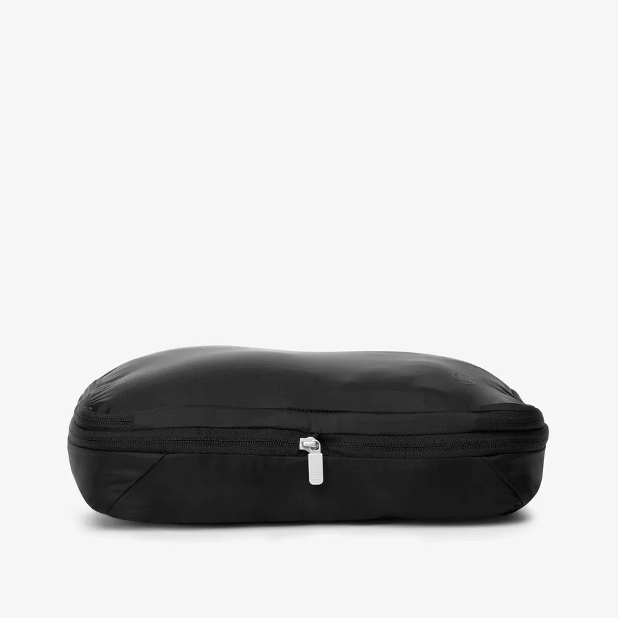The Tortuga Compression Cube in black, a low rectangular compression packing cube with a white zipper pull