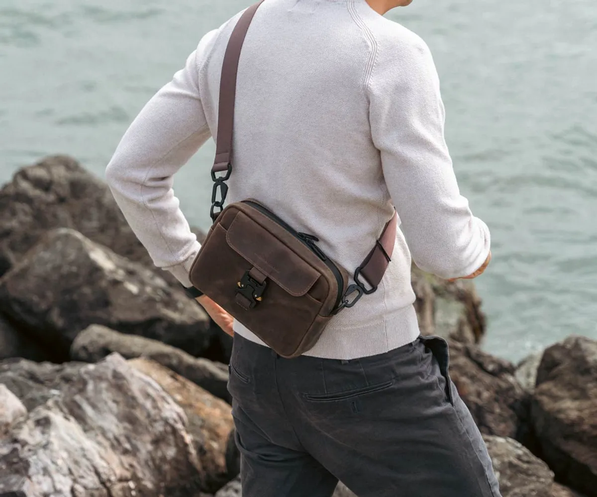A person wearing the brown full-grain leather WaterField Gramercy Leather Sling across the back over a light sweater