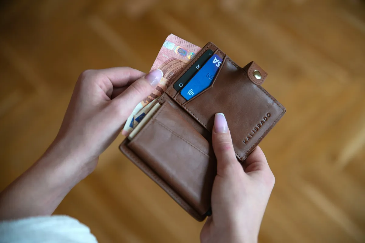 Hands holding a brown leather card wallet with a contactless card and cash
